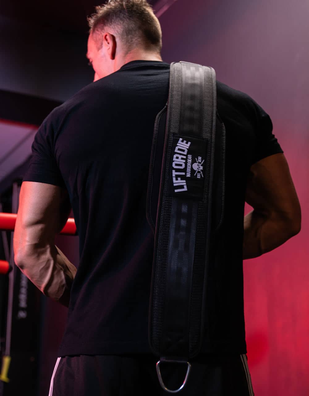 Vista della cintura porta pesi nera Warrior Gear indossata a tracolla, con la toppa Lift or Die e il moschettone di aggancio.