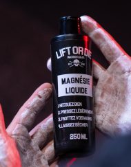 Mains d'un athlète recouvertes de magnésie liquide blanche et sèche, tenant la bouteille Warrior Gear pour la musculation.