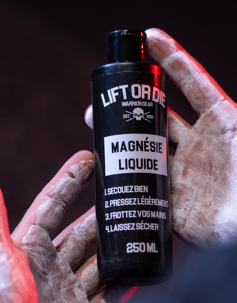 Hands of an athlete covered in dry, white liquid chalk, holding the Warrior Gear bottle for bodybuilding.