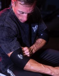 Athlète ajustant une bande de compression noire pour coude et tendinite Warrior Gear sur le biceps.
