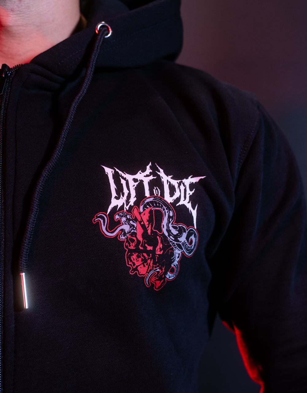 Zbliżenie na nadruk przedstawiający czerwonego węża i czaszkę na klatce piersiowej oraz wykończenie zapinanej na suwak bluzy z kapturem Warrior Gear.