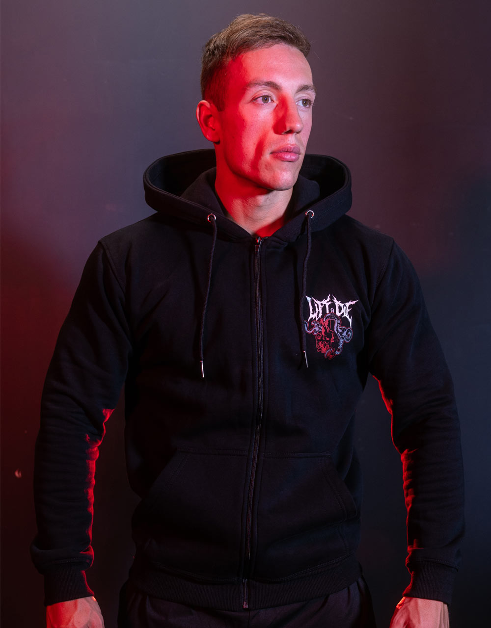 Sportowiec zwrócony twarzą do przodu, ubrany w czarną, rozpinaną bluzę kulturystyczną Warrior Gear z małym logo Lift or Diena piersi.