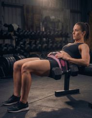 Femme réalisant un hip thrust avec haltères et la ceinture de hip thrust rose pailletée Warrior Gear en salle de sport.
